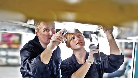 Mann und Frau mit Lampe kontrollieren Unterboden von Fahrzeug.