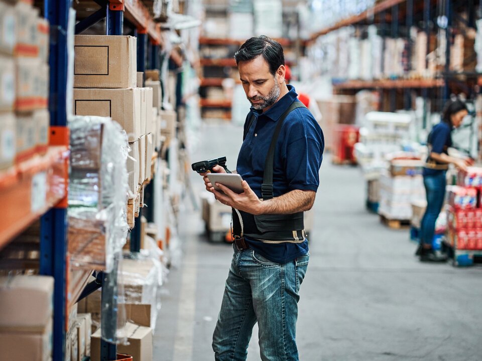 Mann mit Scanner und Tablet im Regallager.