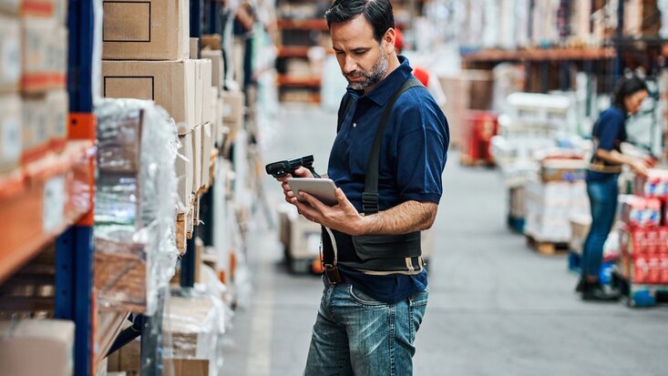 Mann mit Scanner und Tablet im Regallager.