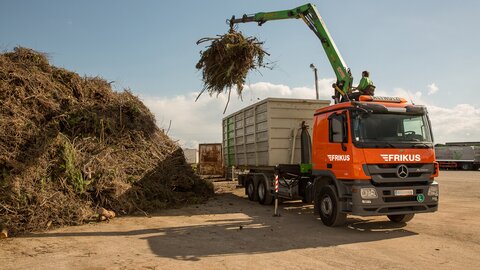Mann entsorgt Holz mit Kran auf Lkw.