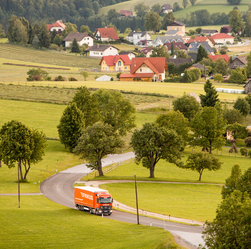 Lkw auf Landstraße Häuser im Hintergrund.