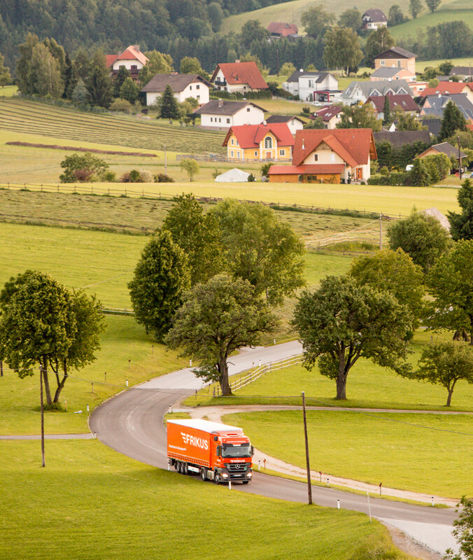 Lkw auf Landstraße Häuser im Hintergrund.