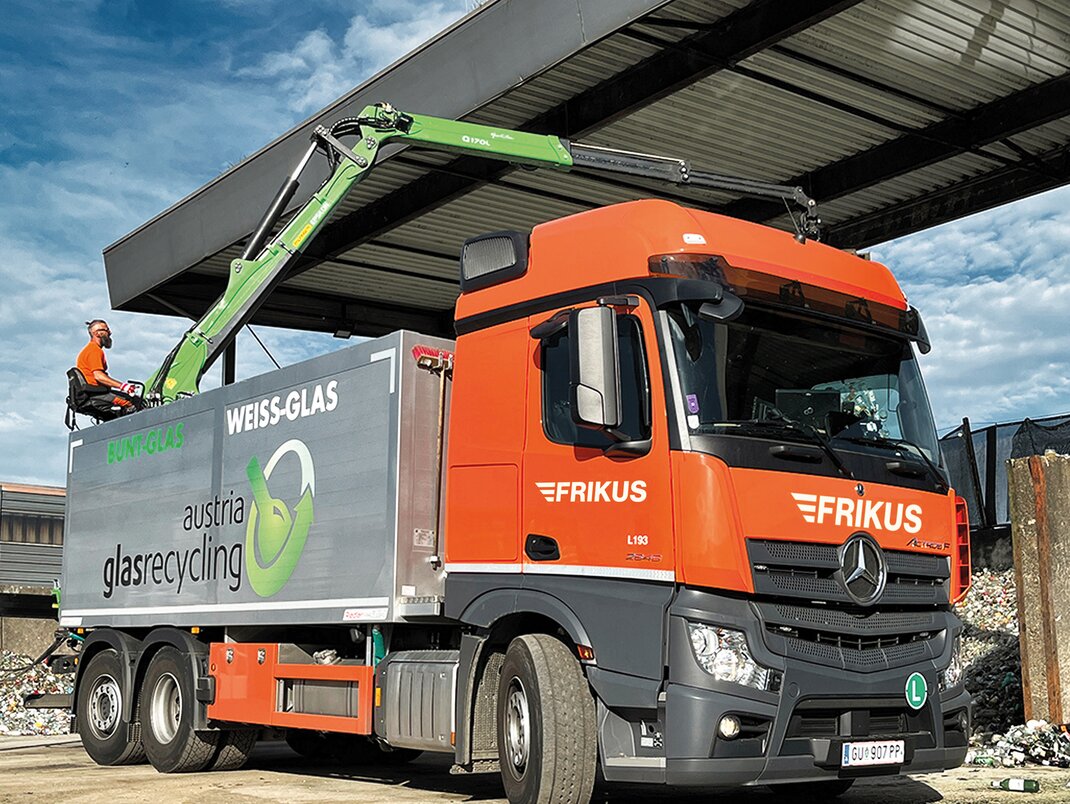 Mann am Kran belädt Lkw mit Altglas. 