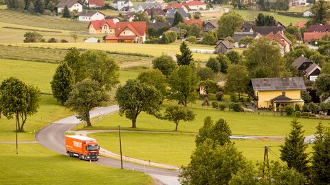 Lkw auf Landstraße Häuser im Hintergrund.